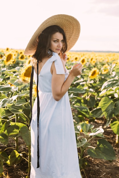 brunette girl in an elegant summer outfit and straw hat in the rays of the sun on nature walk