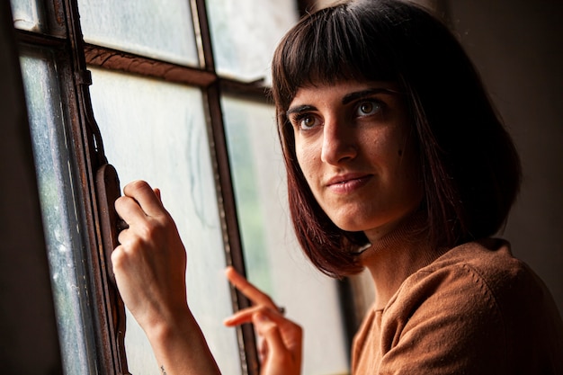 Brunette girl in front of a window looking at the camera, image in low light