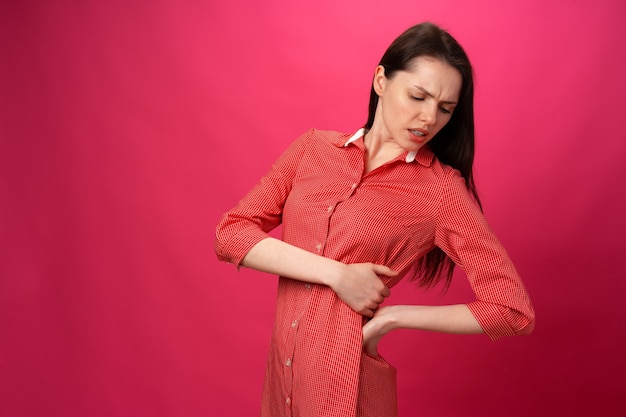 Brunette girl got back pain against pink background