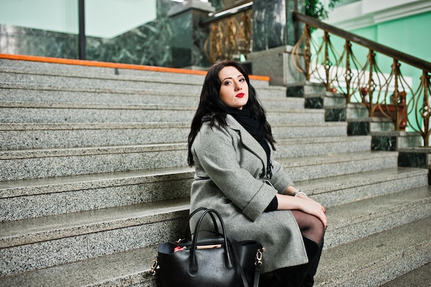 Brunette girl in gray coat posed in stairs of railway station indoor