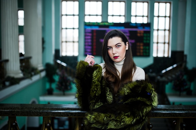 Brunette girl in green fur coat in old hall with column and railings