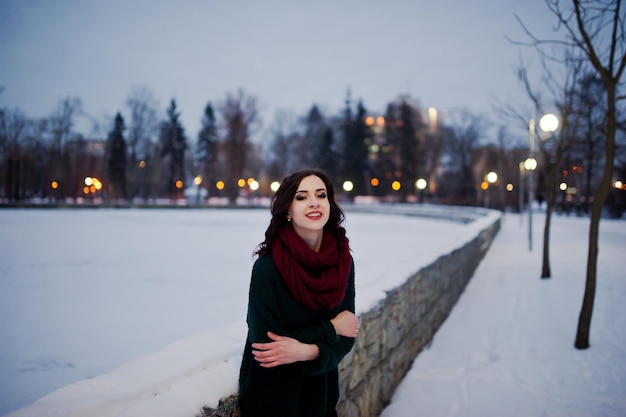 Brunette girl in green sweater and red scarf outdoor on evening winter day