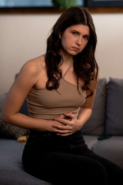 Photo brunette girl has abdominal pain young woman touching her belly with upset face expression