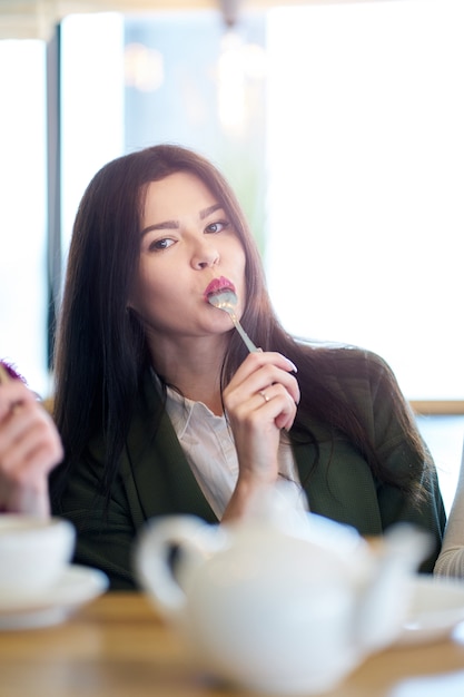 Brunette girl holding spoon in mouth enjoying meal in cafe