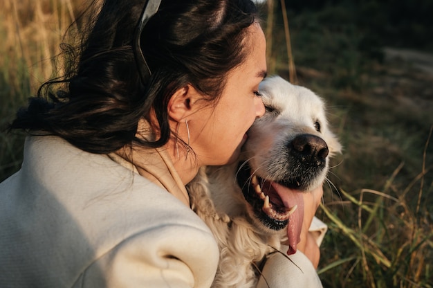 brunette girl hugging white golden retriever in the field