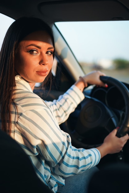 写真 車を運転する縞模様のシャツとジーンズのブルネットの少女