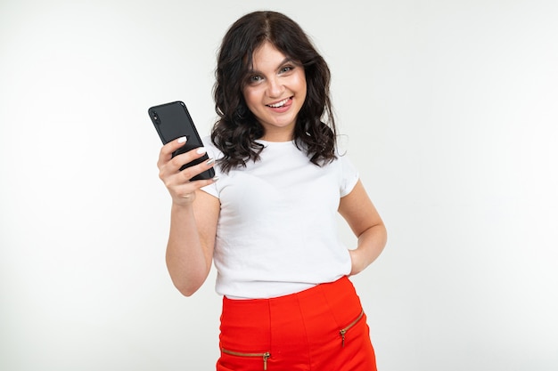 Brunette girl is surfing the internet holding a phone in her hands on a white isolated background