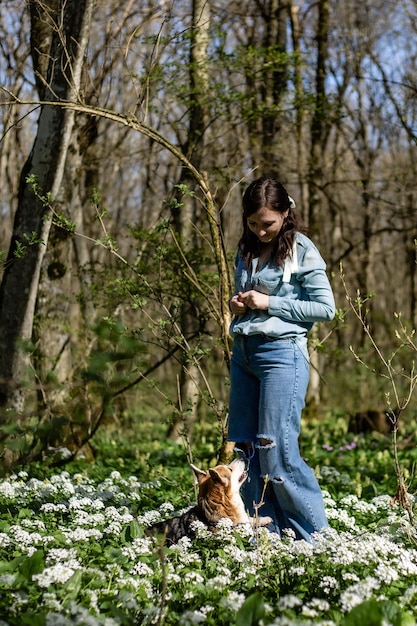 a brunette girl in jeans and a denim shirt on a walk in the woods with a corgi dog