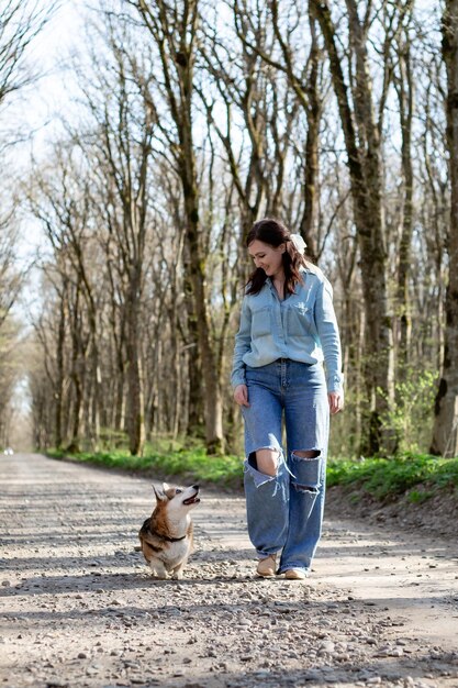 a brunette girl in jeans and a denim shirt on a walk in the woods with a corgi dog