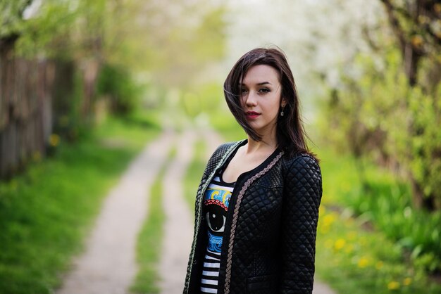 Brunette girl at leather jacket posed on spring garden