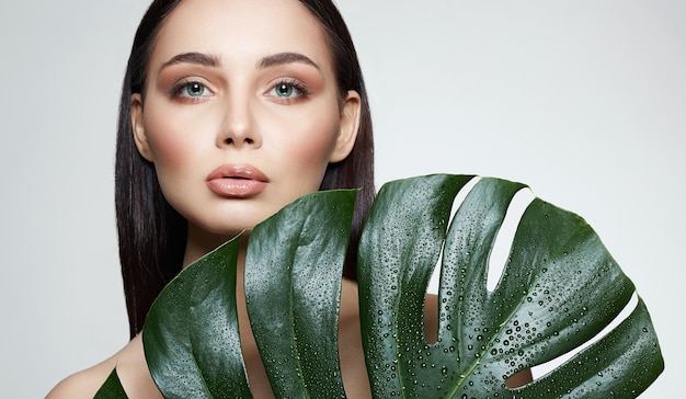 Брюнетка в пальмовых листьях Красивая молодая женщина с макияжем