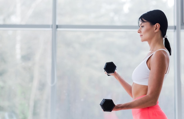 A brunette girl poses with dumbbells in her hands in front of the window Winter weather outside