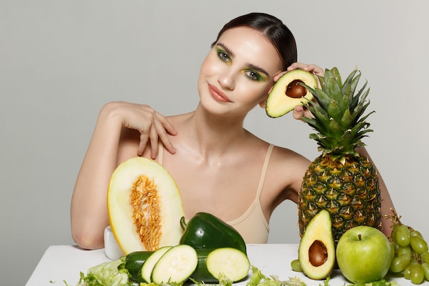 brunette girl posing with table of fruits and vegetables