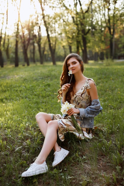 brunette girl sitting on the grass in the evening on a summer walk