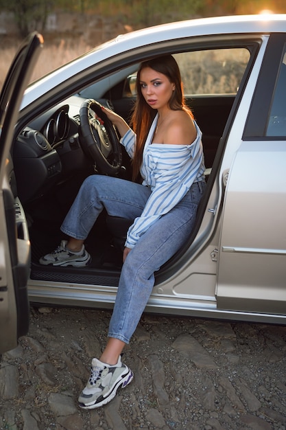 brunette girl in a striped shirt and jeans driving a car