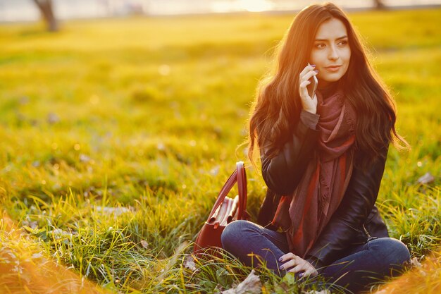 Ragazza bruna usando il suo telefono mentre si sta rilassando al parco durante l'autunno