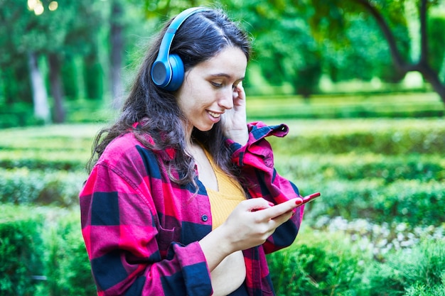 ヘッドフォンで音楽を聴いて公園の庭園を歩くブルネットの少女