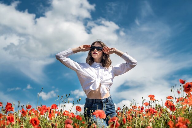 Brunette girl in white blouse walking along a poppy field. summer lifestyle