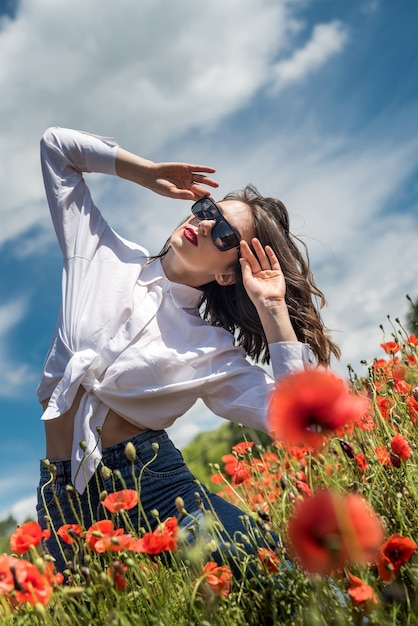 Brunette girl in white blouse walking along a poppy field. summer lifestyle