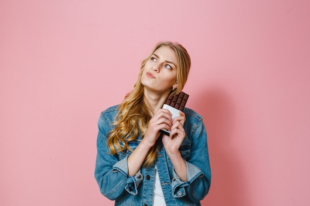 ピンクの背景の上にその味を嗅ぐチョコレートを手に持つブルネットの少女