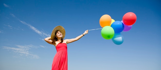 Foto ragazza bruna con palloncini di colore sul cielo blu.