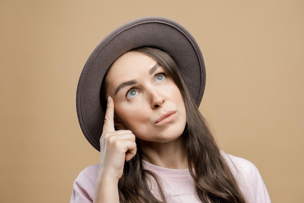 Brunette girl with long hair wearing a hat on a beige background The girl thought about it