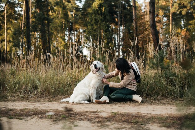 brunette girl with white golden retriever dog on the forest path