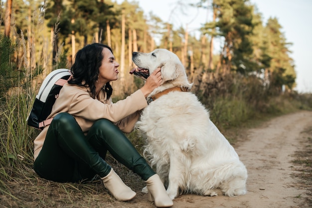 brunette girl with white golden retriever dog on the forest path