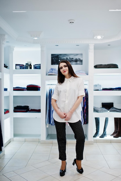 Brunette gorgeous girl in the clothing store boutique at casual clothes white blouse and black pants