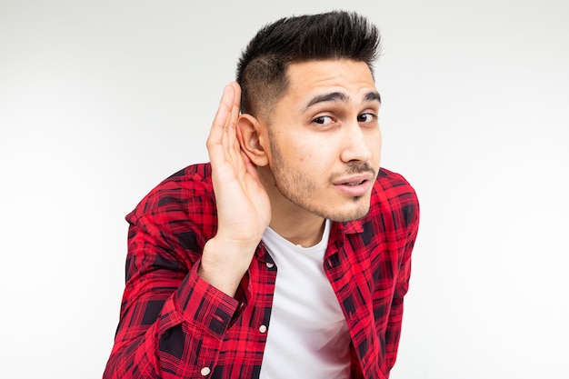 Brunette guy in a checkered shirt wide open eavesdrops on a conversation on a white studio background