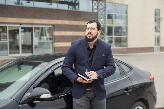 A brunette guy with a beard near a black car