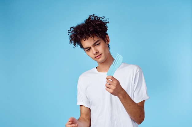 Brunette guy with curly hair on a blue background and a comb in his hand