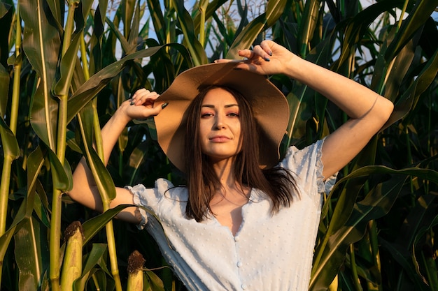 Brunette in blauwe jurk en hoed poseren in cornfield