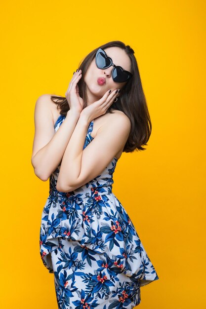 Brunette in een jurk en zonnebril op een gele achtergrond