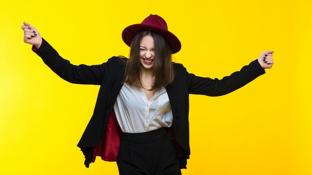 Brunette in een pak en hoed dansen op een gele achtergrond