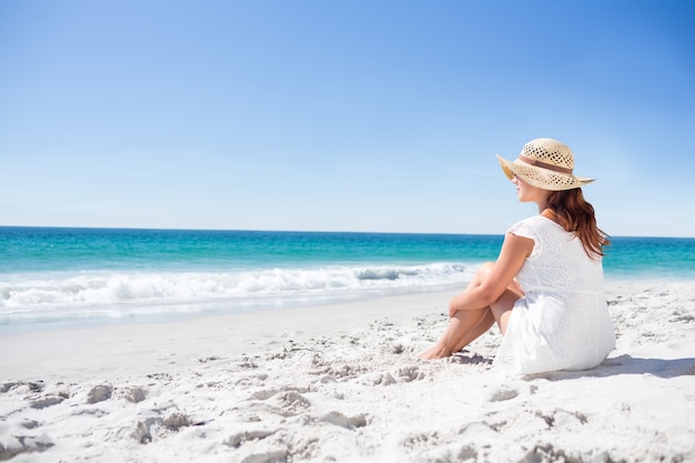 Brunette in het zand zitten en kijken naar de zee