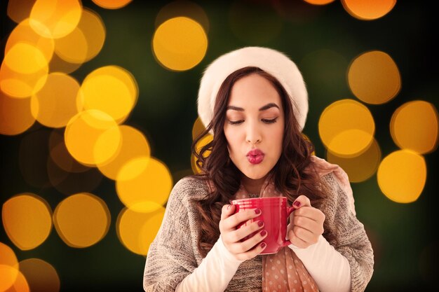 Brunette in winterkleren met warme drank tegen wazige gele kerstlichtcirkels