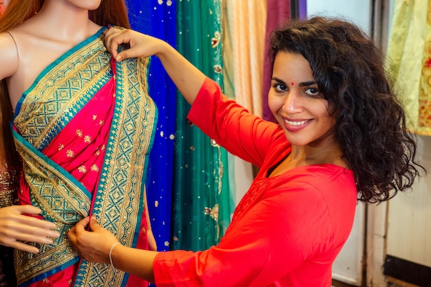 Photo brunette indian woman choosing a new tradition saree in marketneedlewoman designer drapery fabric dress on a mannequin