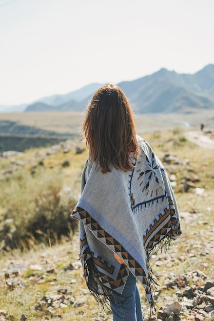 Brunette jonge vrouw reiziger in poncho van terug op road trip naar de bergen Altai