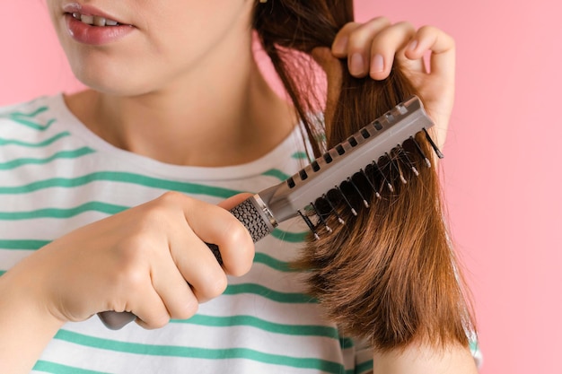 Brunette kamt haar lange haar met een massagehaarborstel, close-up op een roze achtergrond