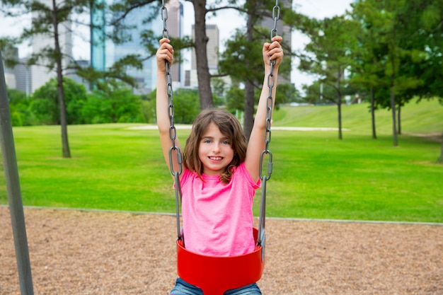 Brunette kid girl playing with swing on city park