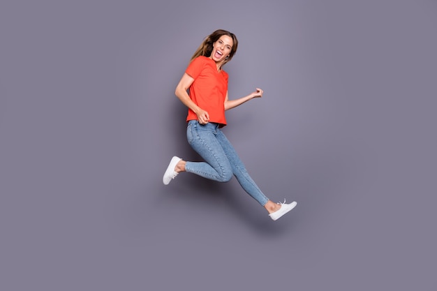 brunette lady in red t-shirt posing and jumping against the purple wall