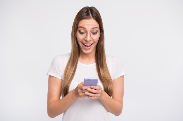 brunette lady with glasses posing against the white wall with her phone