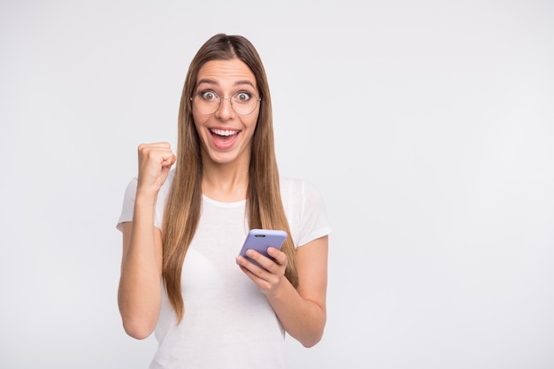 brunette lady with glasses posing against the white wall with her phone