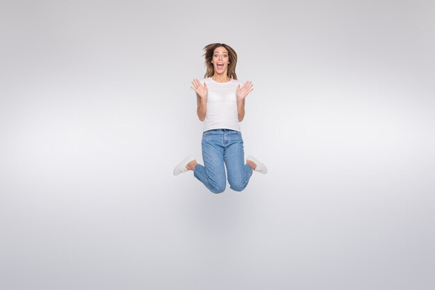 brunette lady with glasses posing and jumping against the white wall
