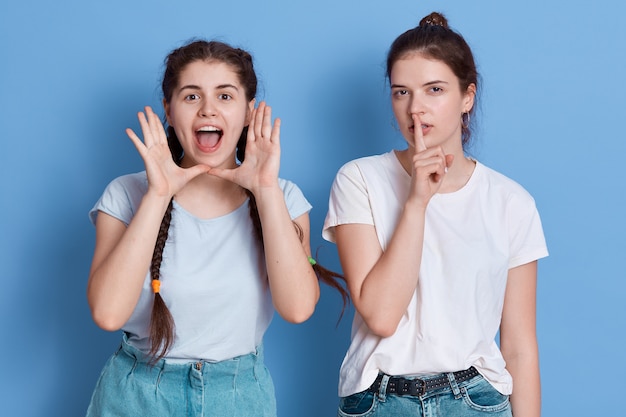 Brunette lady with hair bun refuses to listen to cry of her friend and keeps finger near lips