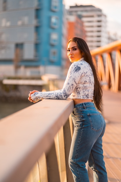 A brunette Latin girl in jeans in the city at sunset