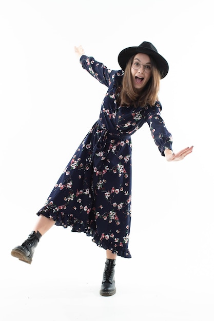 A brunette in a long floral dress with a hat poses for the camera in the studio. Emotional portrait