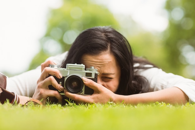 Brunette lying on grass taking picture with retro camera 