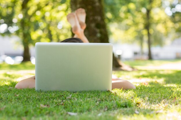 Photo brunette lying on the grass typing at her laptop